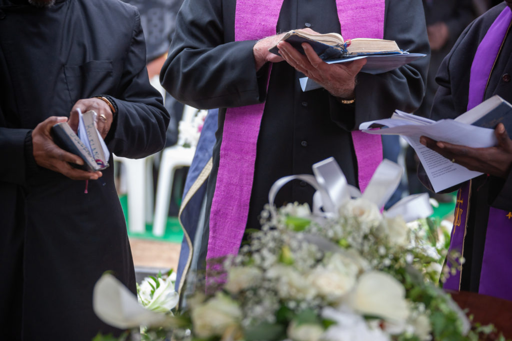 Priester auf einer Beerdigung, neben dem Grab